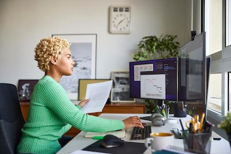 Young women in a green dress sitting at a desk looking at her computer while she works from home