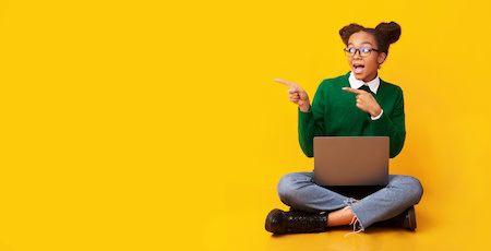young woman sitting down in front of a yellow background with a laptop in her lap - best free online colleges in Nevada