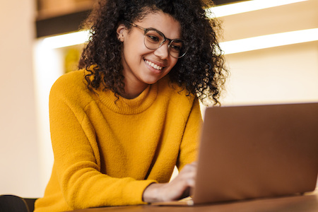 young woman smiling while working on her laptop - best free online colleges in Minnesota