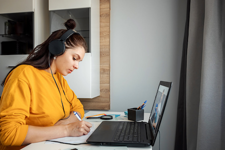 young woman taking notes while watching a college course lecture on her laptop - best low-cost and free online colleges in South Dakota