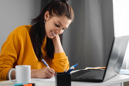 young woman taking notes while working on her laptop - best free online colleges in New Hampshire