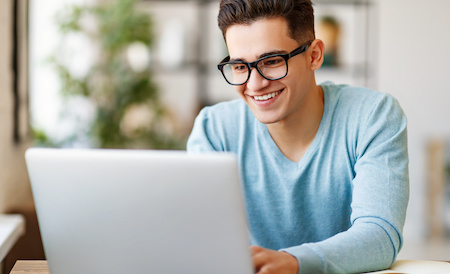 young man working on his laptop computer at a desk - best free online colleges in Maine