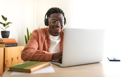 young man smiling while he works on his laptop - best free and cheap online colleges in South Carolina