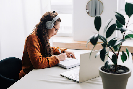 young women wearing headphones and taking notes at her desk